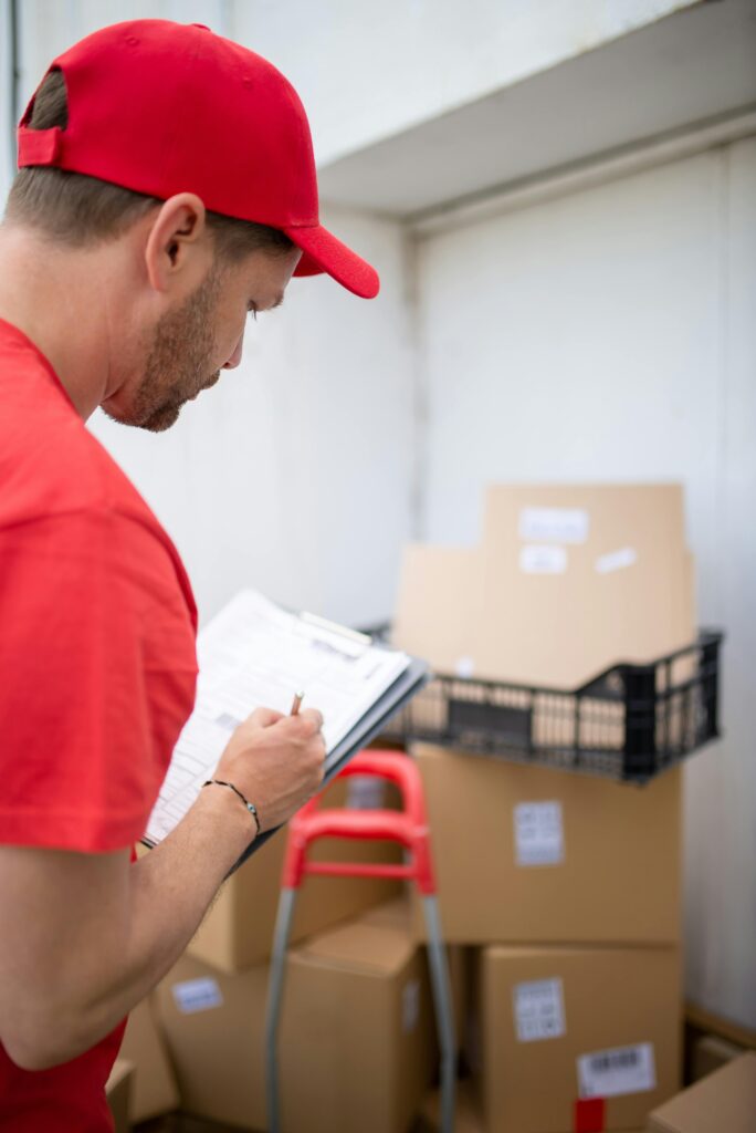 pexels photo 7843990 7843990 A courier in a red uniform checks inventory in a warehouse setting.